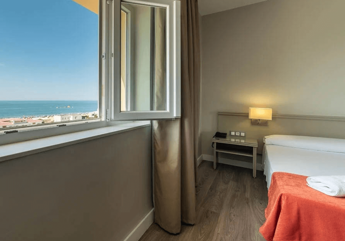 Acogedora habitación de hotel Pato: Corporativa con ventana abierta y vista al mar y playa.