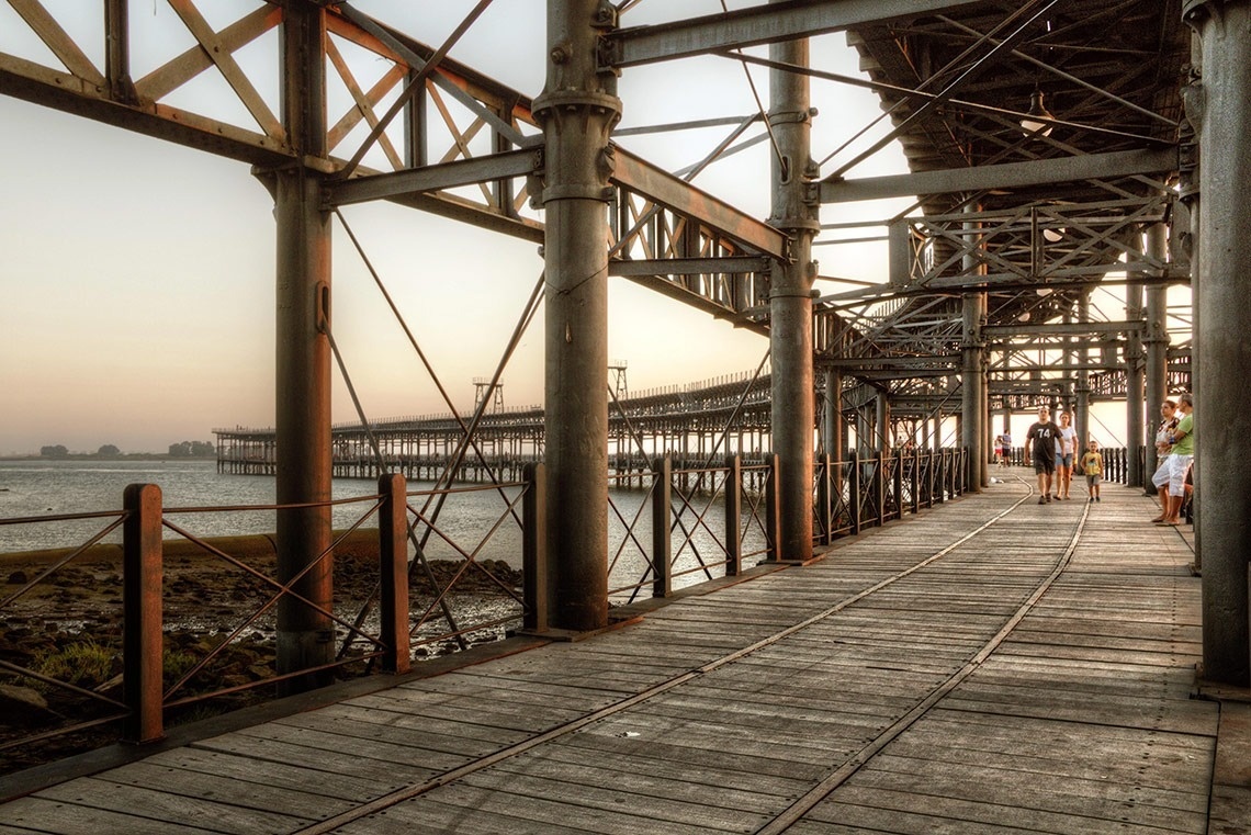 Passeio histórico no cais metálico ao pôr do sol, vista panorâmica. Ideal para experiências Pato Corporativa.