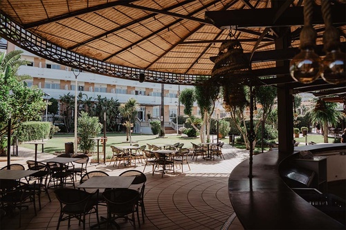 Hotel Pato Amarillo: Área exterior com mesas e cadeiras sob um telhado de palha, vista para o jardim e o hotel.