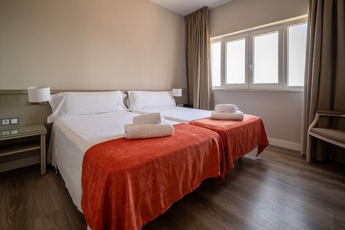 Twin bedroom at Pato Rojo Hotel in Punta Umbria with bright window, white beds, and orange throws.