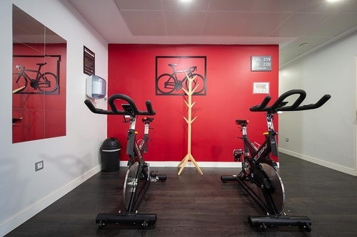 Modern Pato Rojo Hotel fitness room with two spin bikes, red wall, and bicycle art, ideal for your stay in Punta Umbria.