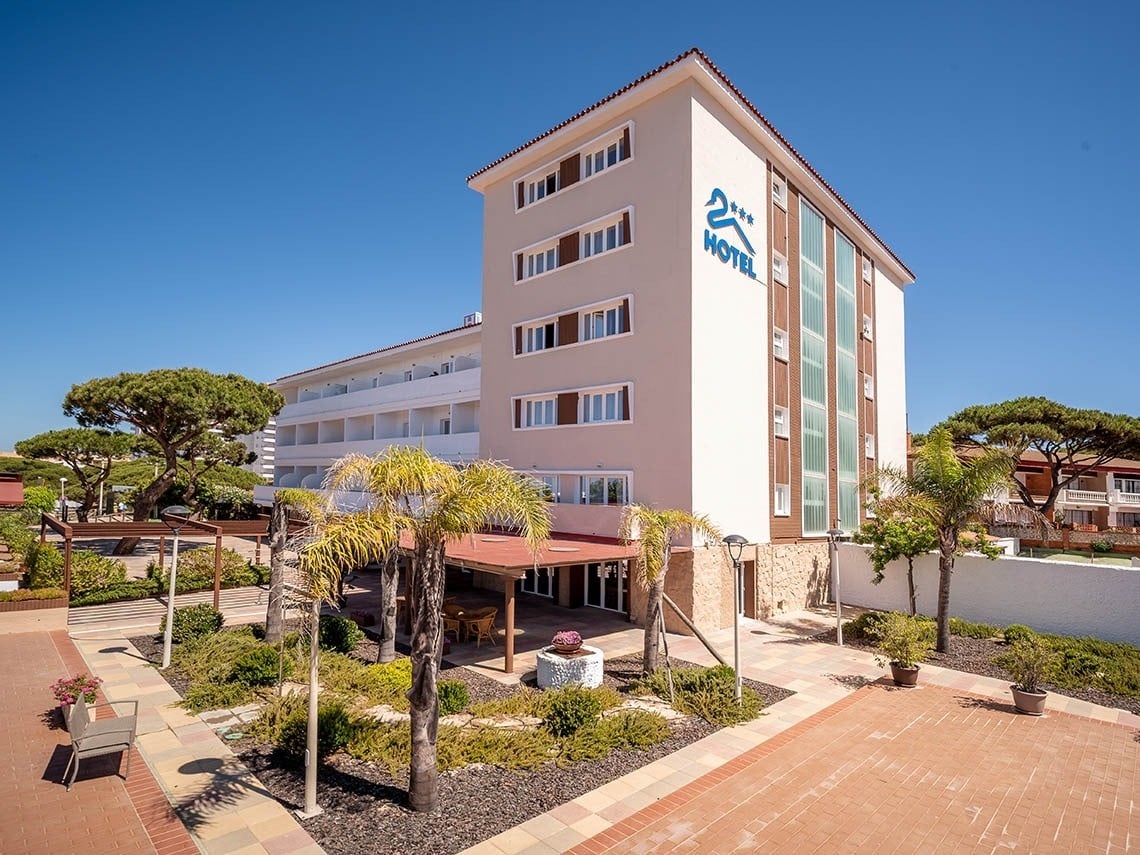 Hotel Pato Rojo en Punta Umbría, Huelva: exterior con jardines, palmeras y cielo azul. Web oficial.
