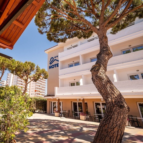 Sunny exterior of Pato Rojo Hotel in Punta Umbria, with balconies, a patio, and a prominent tree.
