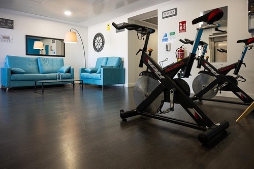 Pato Rojo Hotel in Punta Umbria: Modern lounge with turquoise sofas and a fitness area with spinning bikes.