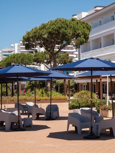 Pato Rojo Hotel outdoor patio with blue umbrellas and modern chairs under a clear sky in Punta Umbria.