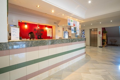 Pato Rojo Hotel reception desk in Punta Umbria lobby. Staff member behind a modern desk with striped tiles and red wall.