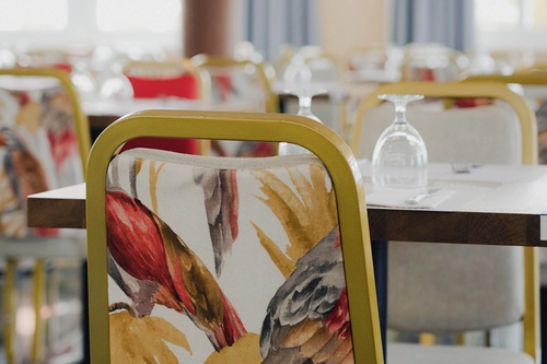 Decoração vibrante no Hotel Pato Amarillo: cadeiras com estampa de pássaros e toalhas de mesa postas.