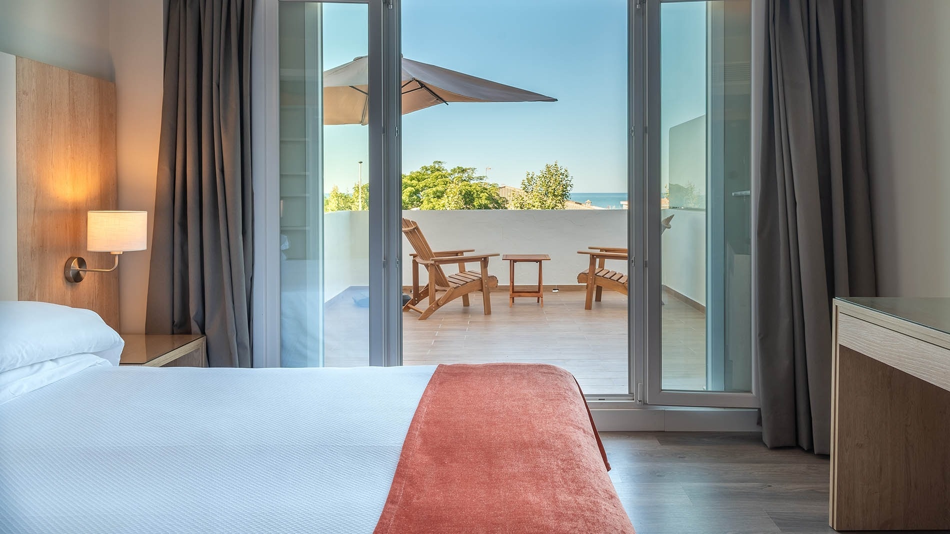 Habitación de Hotel Pato Rojo con cama, balcón privado, sillas de madera y vistas al mar en Punta Umbría.