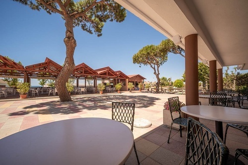 Pato Rojo Hotel, Punta Umbria: Sunny outdoor cafe patio with trees, covered seating, and sea views.