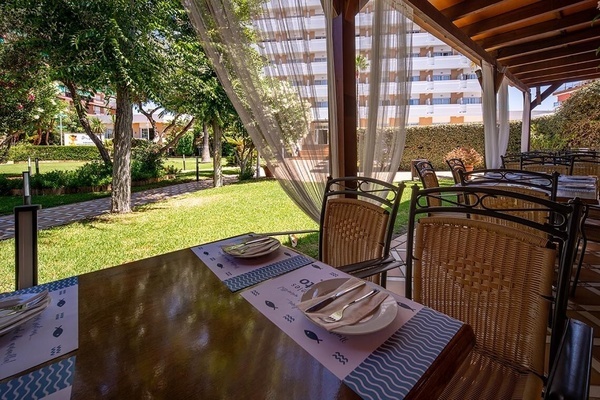 Pato Corporativa hotel outdoor dining area with lush garden views and set tables.