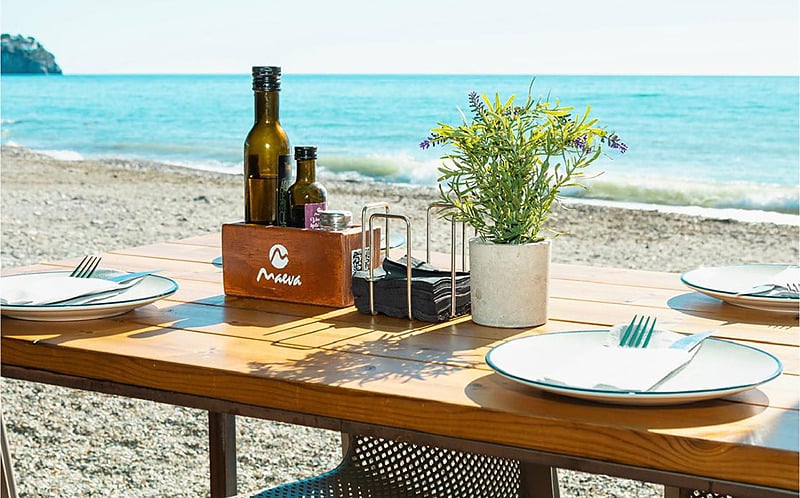 Mesa junto al mar con platos,Pena Parda servilletas y botellas, con vistas al océano.
