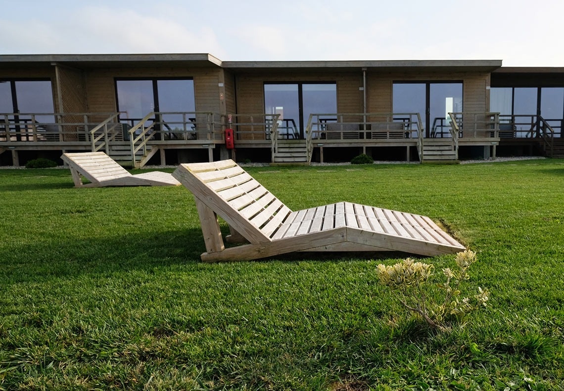 duas espreguiçadeiras de madeira estão sentadas na grama em frente a uma casa