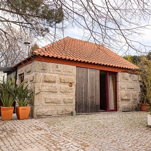 uma pequena casa de pedra com um telhado vermelho e uma porta vermelha