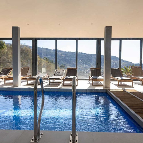 Piscina interior de hotel com vista panorâmica para montanhas e espreguiçadeiras.