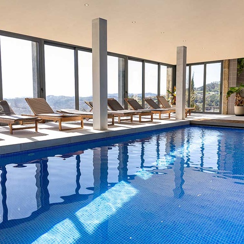 Piscina interior de hotel com vista panorâmica da montanha e espreguiçadeiras.