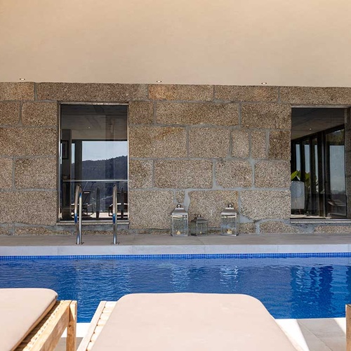 Piscina coberta de hotel com paredes de pedra, espreguiçadeiras e vista para a natureza.