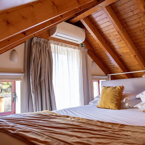 Quarto de hotel em sótão com teto de madeira, cama confortável, janelas e ar condicionado.