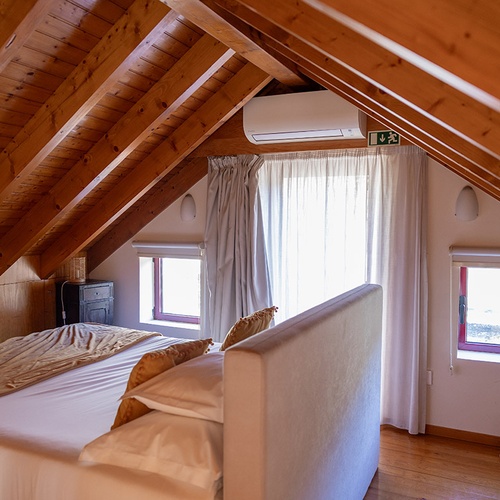 Quarto de sótão acolhedor em hotel com teto de madeira, cama, janelas claras e ar condicionado.