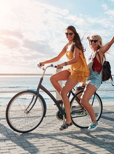 two young women are riding bicycles on a pier near the ocean .