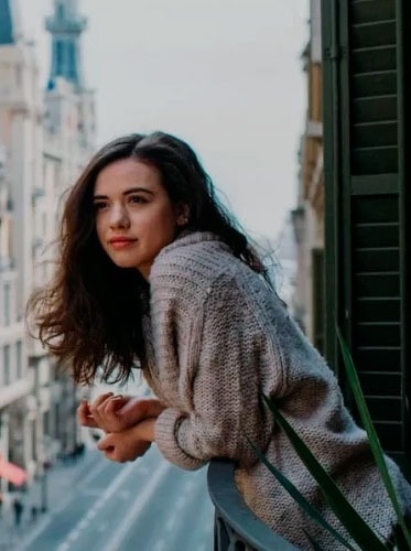 a woman in a sweater is standing on a balcony looking out over a city street .