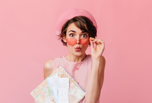 una mujer con sombrero rosa y gafas de sol sostiene un mapa y boletos
