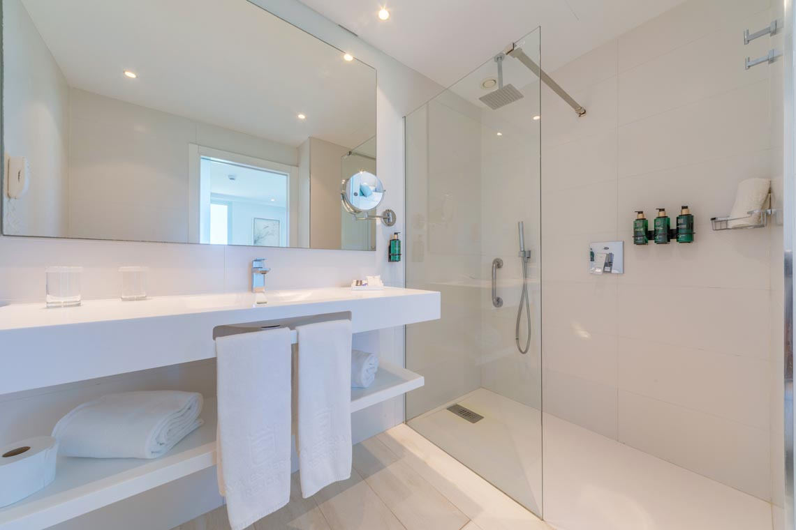 Baño moderno con ducha cristalina, lavabo y toallas limpias. Playa Esperanza Resort.