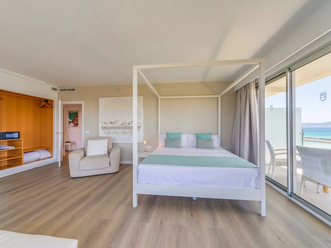 Cama con dosel, armario, sillón y balcón con vista al mar en hotel Playa Esperanza Resort.