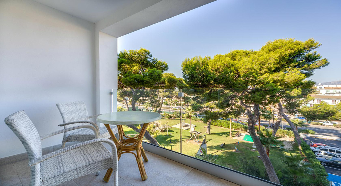 Balcón con sillas y mesa, vista a un parque infantil y árboles exuberantes, ideal para Playa Esperanza Resort.