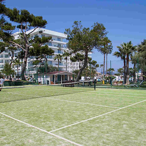 Pista de tenis en el hotel Playa Esperanza Resort con palmeras y un edificio moderno de fondo.