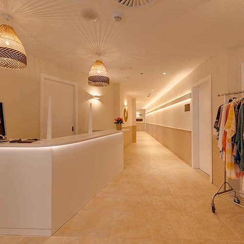 Recepción de hotel con iluminación ambiental, plantas y perchero de ropa, ideal para tu Playa Esperanza Resort.