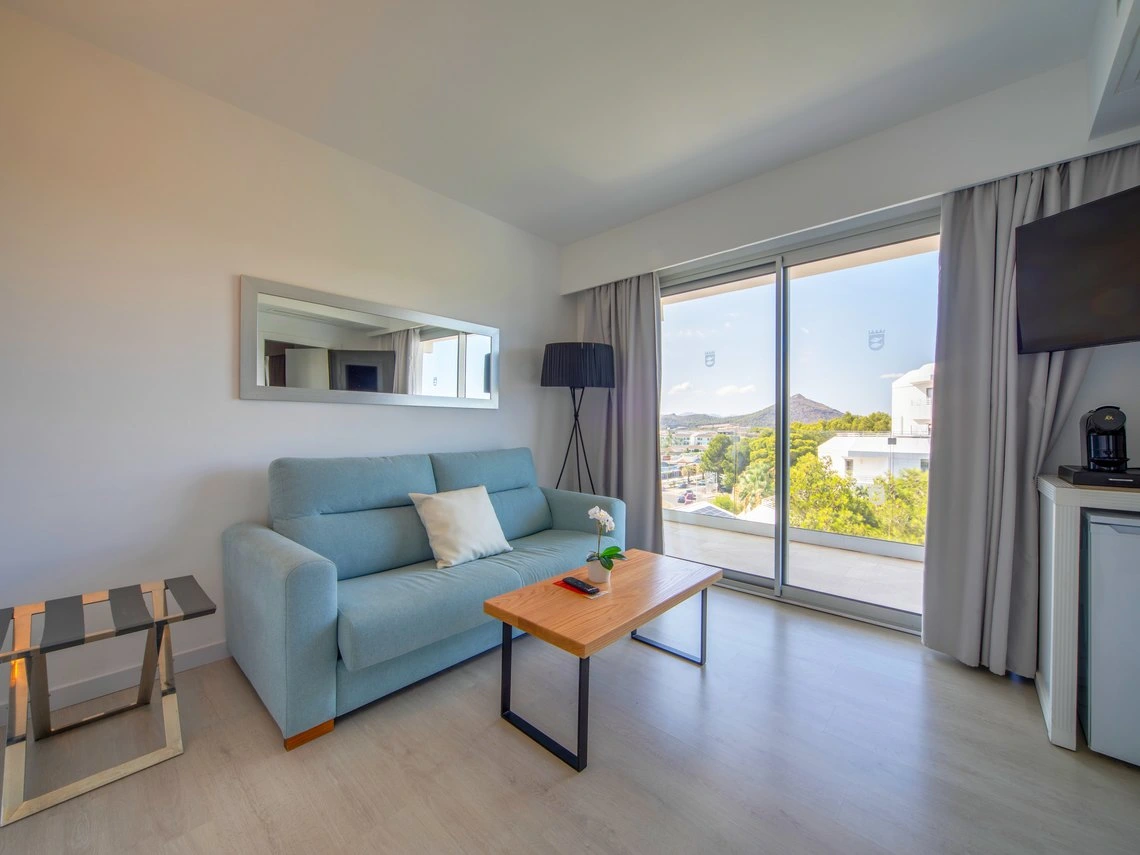 Sala de estar luminosa con sofá azul claro, mesa de centro de madera y vistas al exterior, ideal para Playa Esperanza Resort.