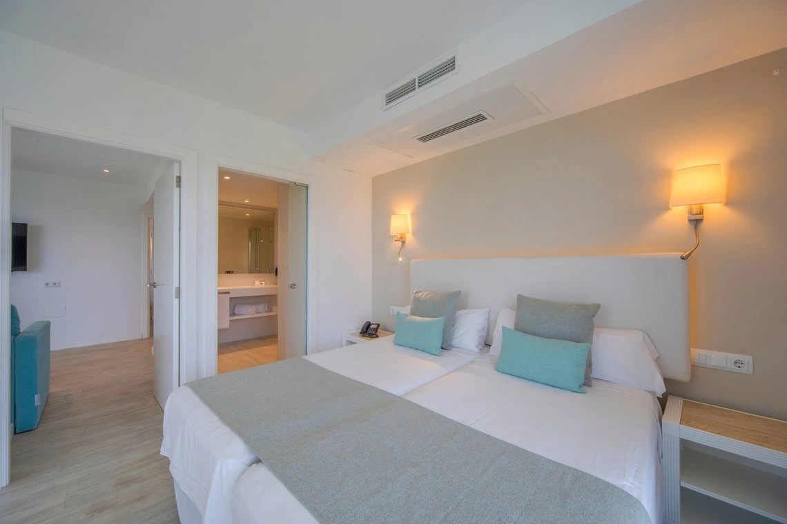 Habitación de hotel luminosa con cama doble, Playa Esperanza Resort, baño y sillón azul.