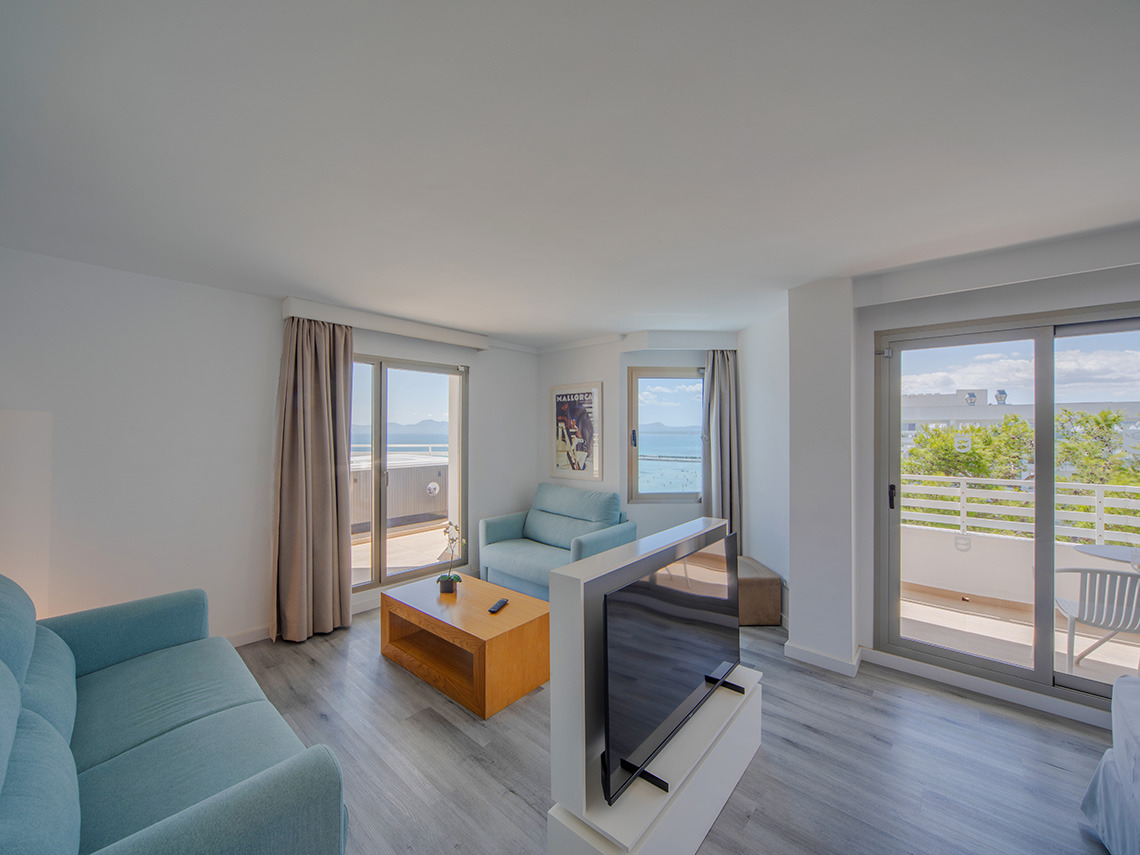Salón luminoso con sofás turquesa, mesa de centro de madera y Playa Esperanza Resort con vistas al mar.