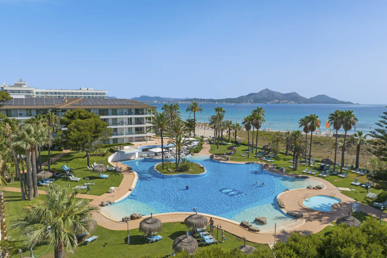 Piscina y playa del hotel con palmeras y mar turquesa.