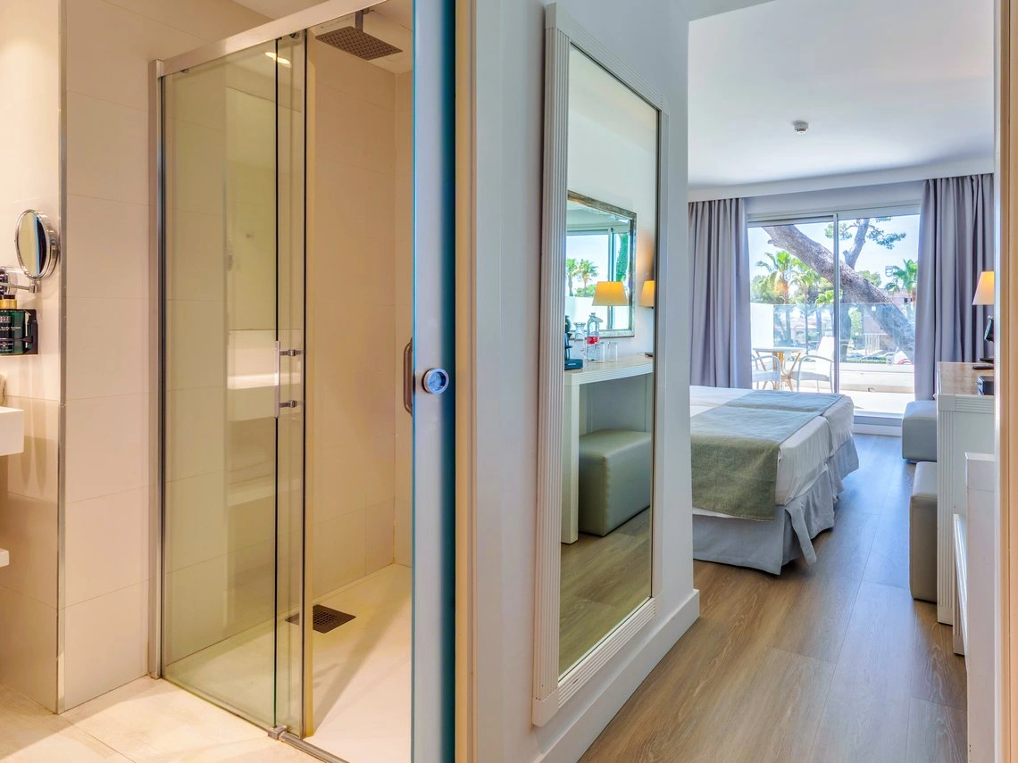 Ducha de cristal y habitación de hotel con cama doble, Playa Esperanza Resort y vistas al exterior.
