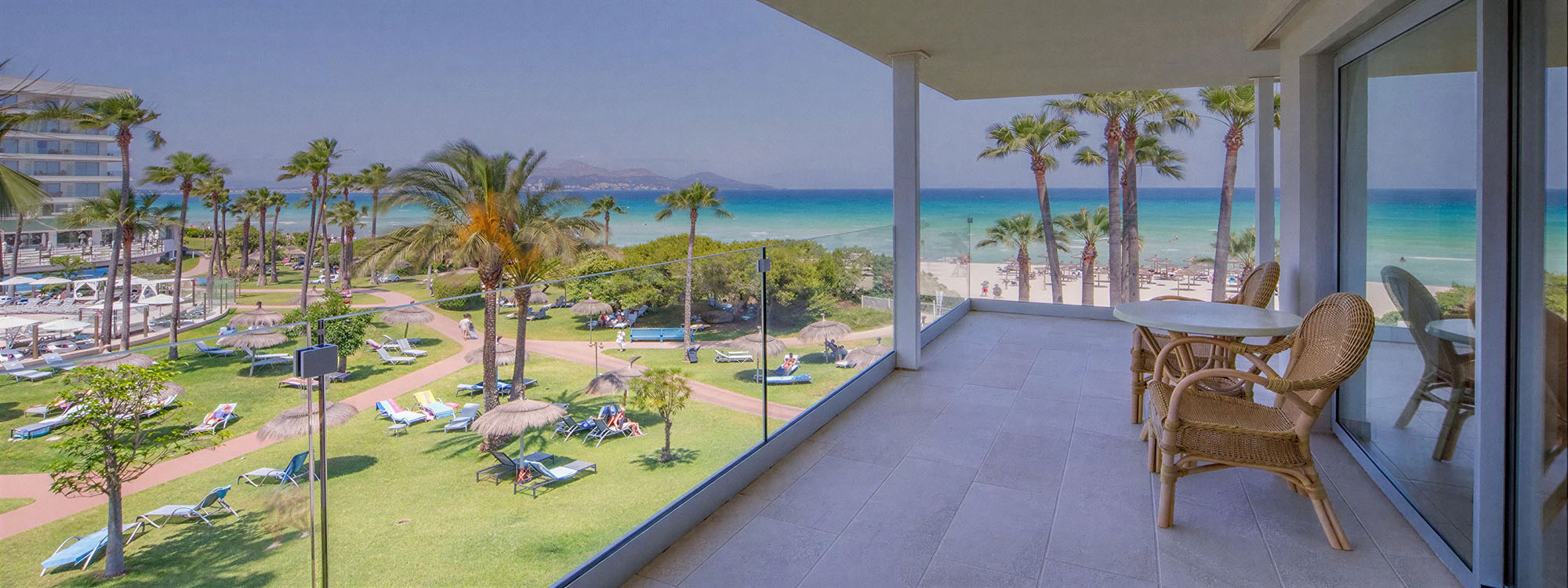 Vista de balcón de hotel a playa tropical, tumbonas, palmeras y mar azul, ideal para Playa Esperanza Resort.