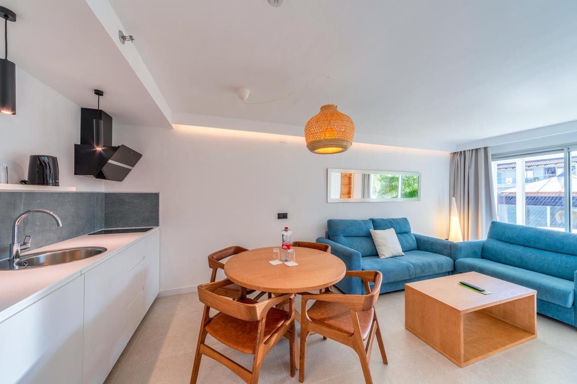 Sala de estar y cocina moderna con sofás azules, mesa de comedor y encimera. Playa Esperanza Resort