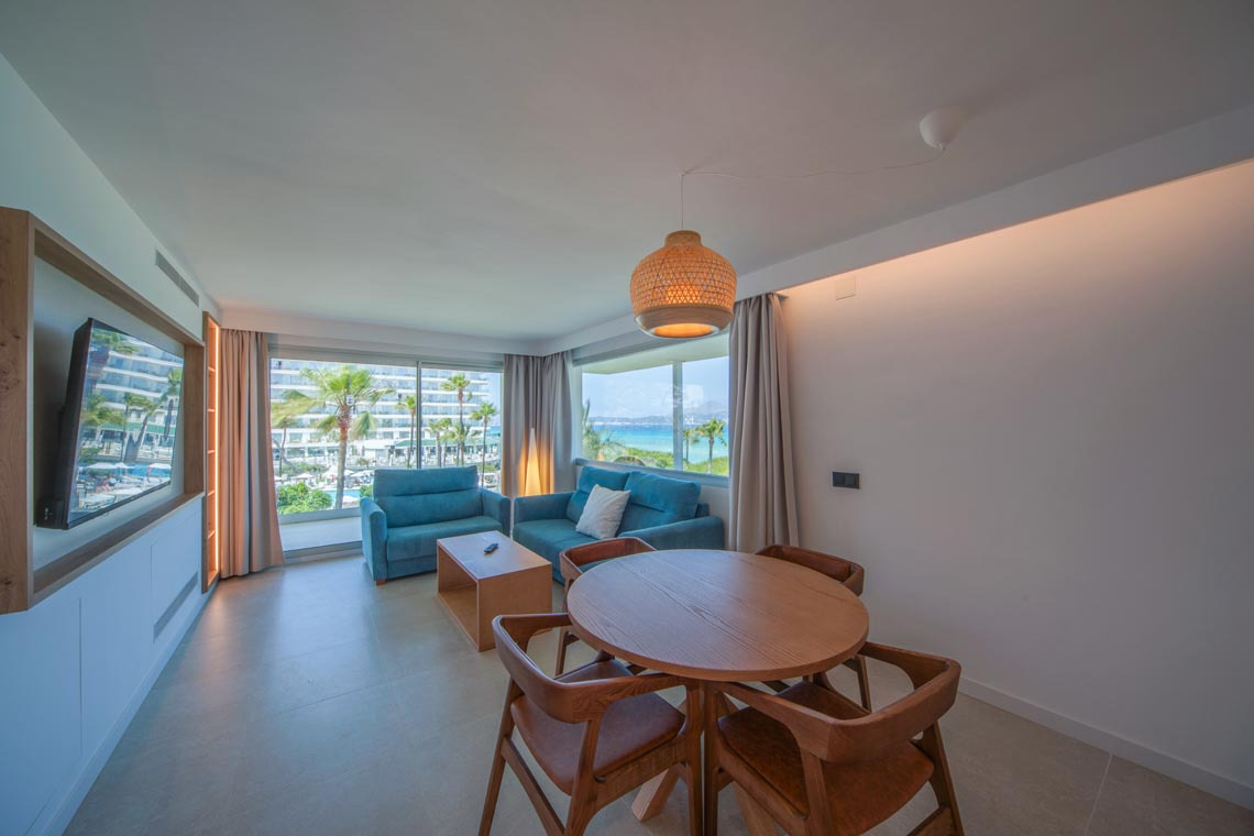 Amplio salón con vistas al mar, sofá azul, mesa de centro y sillas de comedor, ideal para tu Playa Esperanza Resort.