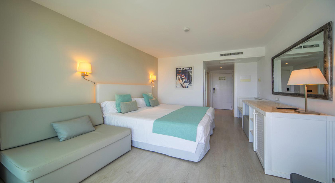 Habitación de hotel moderna con cama, sofá y espejo. Playa Esperanza Resort