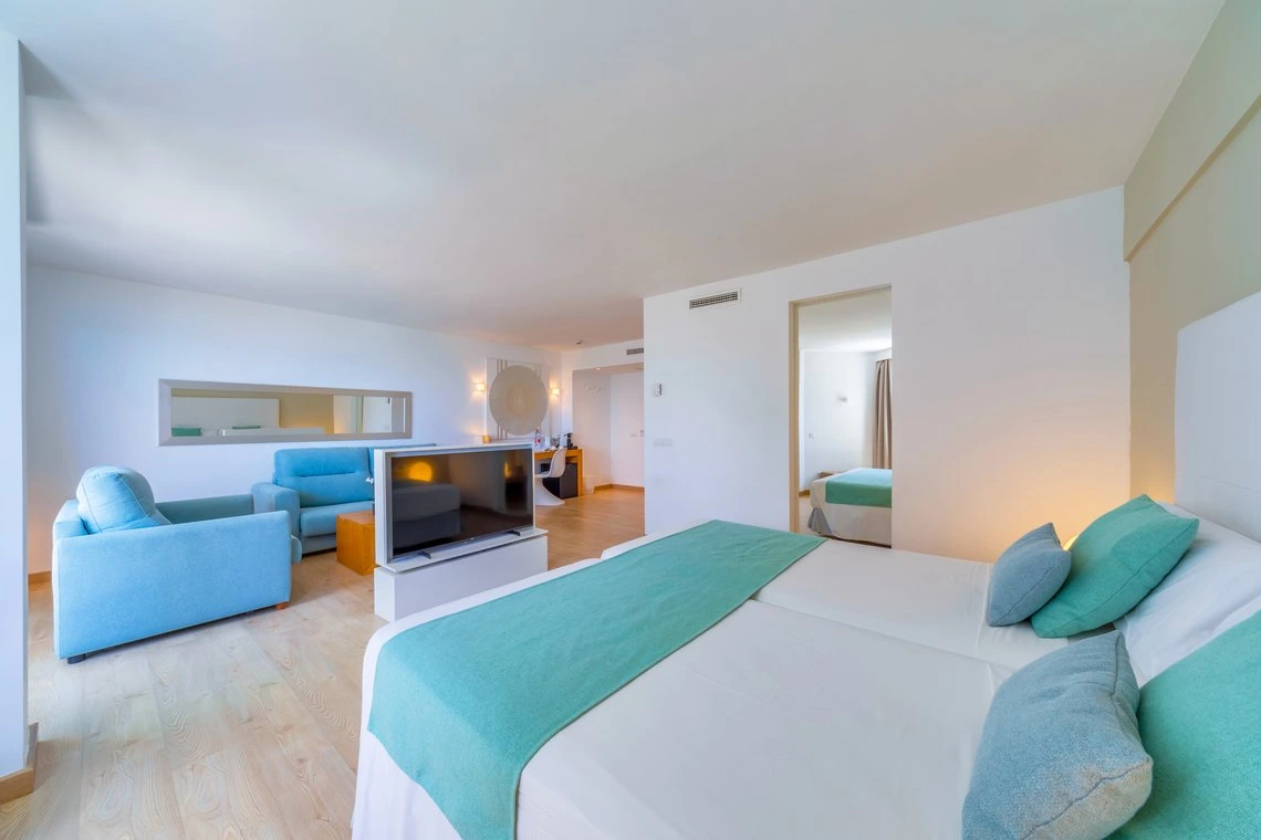 Suite de hotel luminosa con dos camas individuales, sala de estar y vistas a otra habitación con Playa Esperanza Resort.
