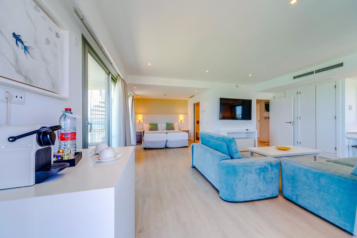 Amplia habitación de hotel con Playa Esperanza Resort, cama, sofá azul y balcón.
