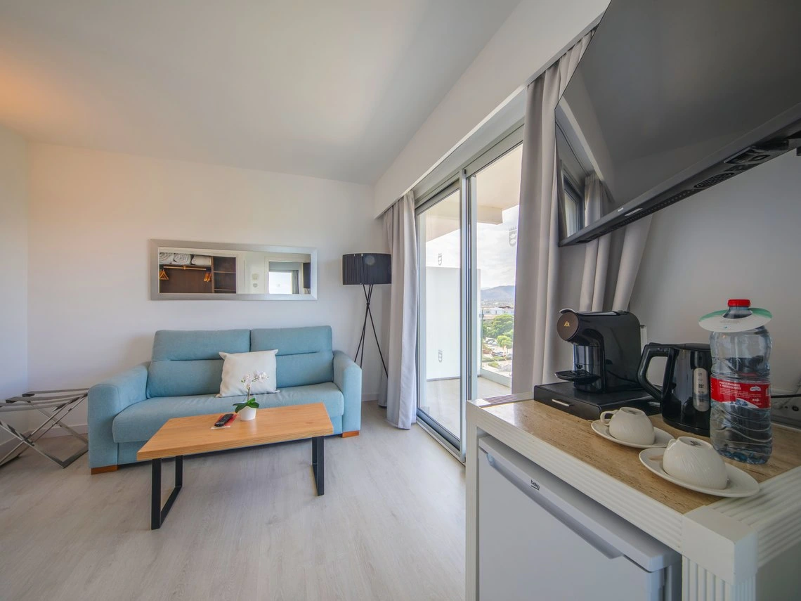 Suite con sofá azul, mesa de centro de madera, cafetera y Playa Esperanza Resort.