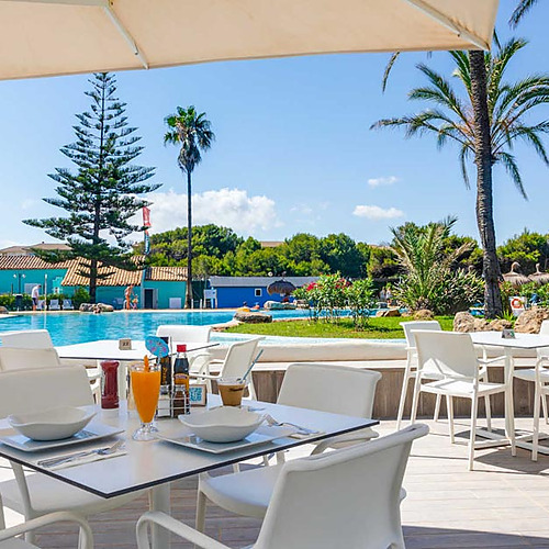 Terraza de restaurante en hotel tropical con piscina, palmeras y mesas listas para servir Playa Esperanza Resort.