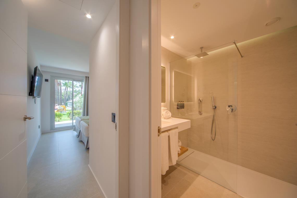 Vista de una suite moderna con cama, terraza y baño con ducha. Playa Esperanza Resort
