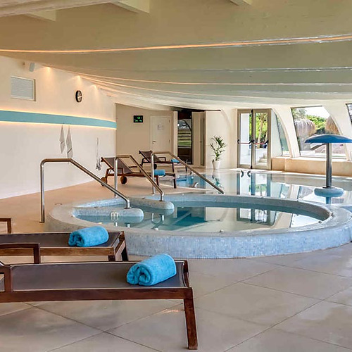 Relajante zona de piscina cubierta con tumbonas, jacuzzis y vistas al exterior, perfecta para tu Playa Esperanza Resort.