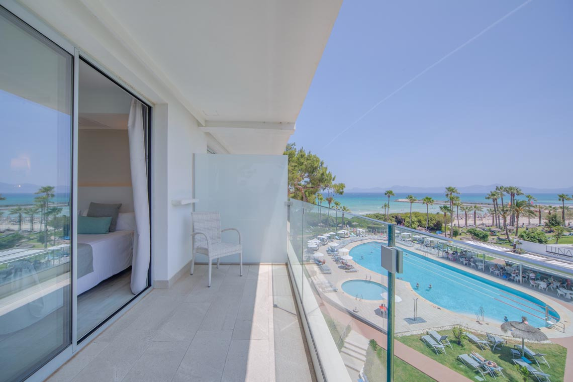 Balcón con vista a piscina y mar, Playa Esperanza Resort de lujo con cama y sillón.