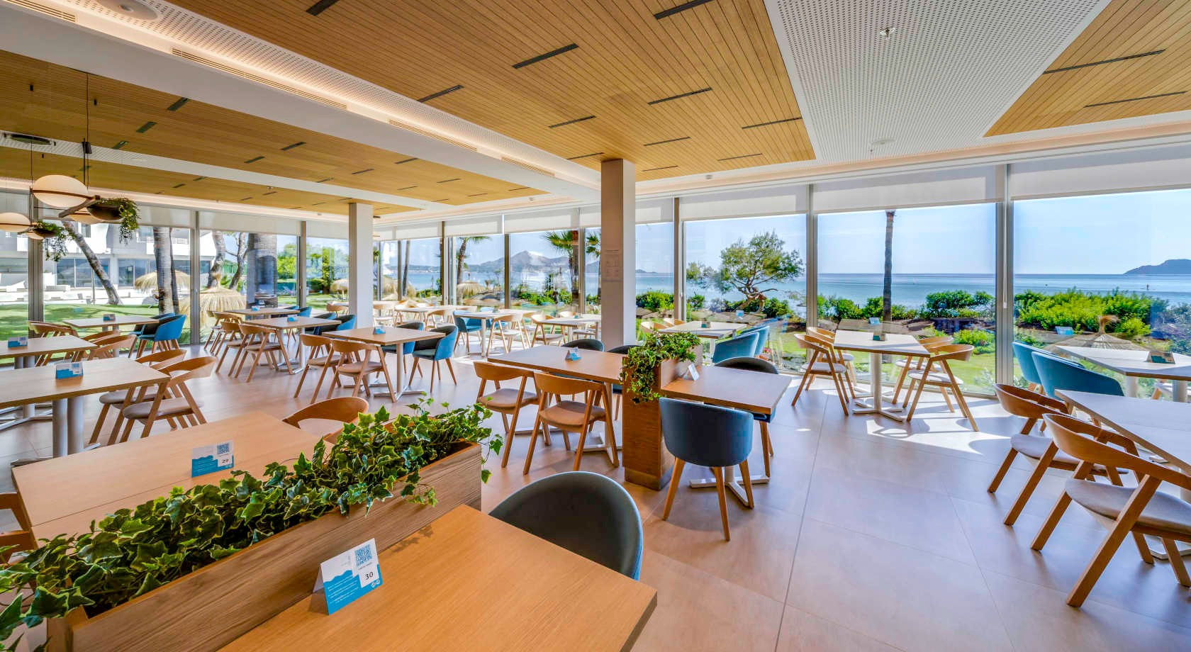 Restaurante de hotel con vista al mar, mesas de madera y sillas modernas. Playa Esperanza Resort