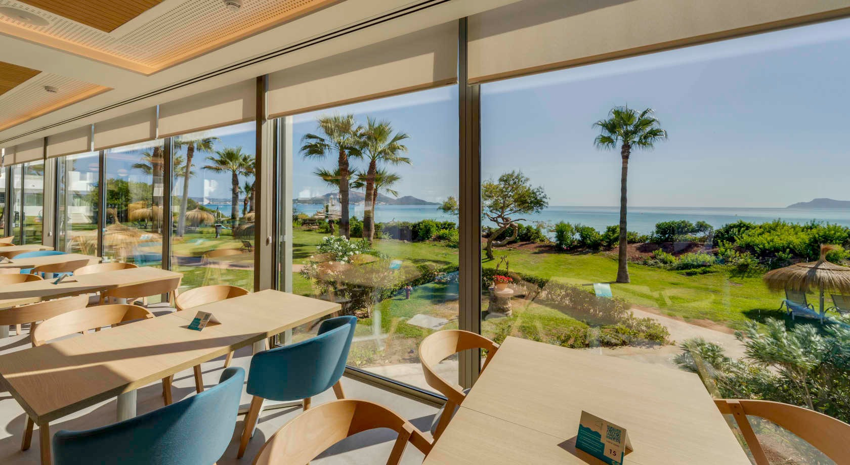 Vista al mar desde el restaurante de Playa Esperanza Resort. Mesas y sillas en interior con terraza ajardinada.