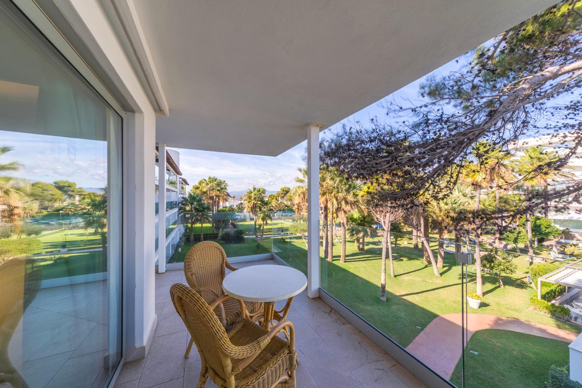 Balcón con mesa y sillas con vista a un exuberante jardín tropical y el mar, ideal para Playa Esperanza Resort.
