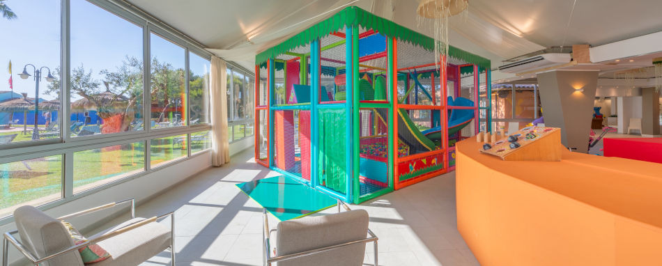 Zona de juegos interior colorida para niños en Playa Esperanza Resort con vistas al exterior.